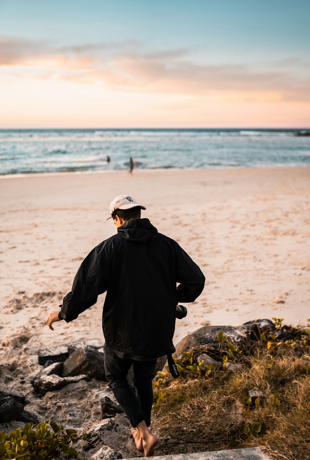 homme en veste noire et casquette grise debout sur le rocher gris près de la mer pendant la journée