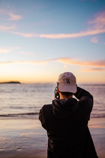 man in black jacket and gray cap standing on beach during daytime