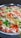 A close-up view of a dish featuring long-grain rice mixed with vibrant colors. Green, orange, and white colors are prominent, suggesting the use of spices or food coloring. The rice appears fluffy and is served in a metal container.