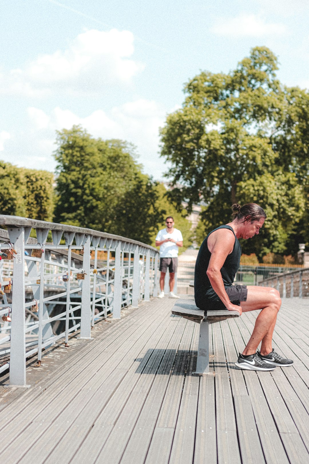 man in pink tank top and black shorts sitting on gray wooden bridge during daytime