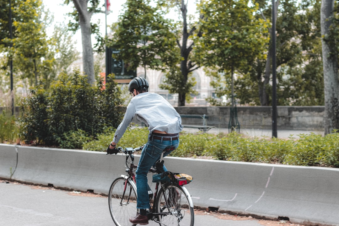 man in white long sleeve shirt and blue denim jeans riding on bicycle on road during