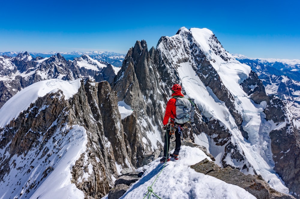 person in red jacket and black pants walking on snow covered mountain during daytime