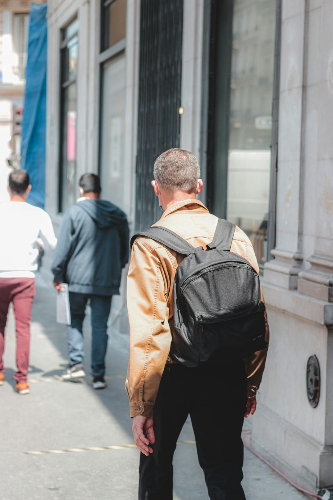 man in blue jacket and brown backpack walking on sidewalk during daytime