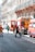 Several fire trucks and emergency personnel in uniforms are present on a city street lined with ornate buildings. A few pedestrians can also be seen walking nearby, and metal barricades are set up, suggesting a controlled or restricted area.