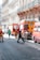 Several fire trucks and emergency personnel in uniforms are present on a city street lined with ornate buildings. A few pedestrians can also be seen walking nearby, and metal barricades are set up, suggesting a controlled or restricted area.