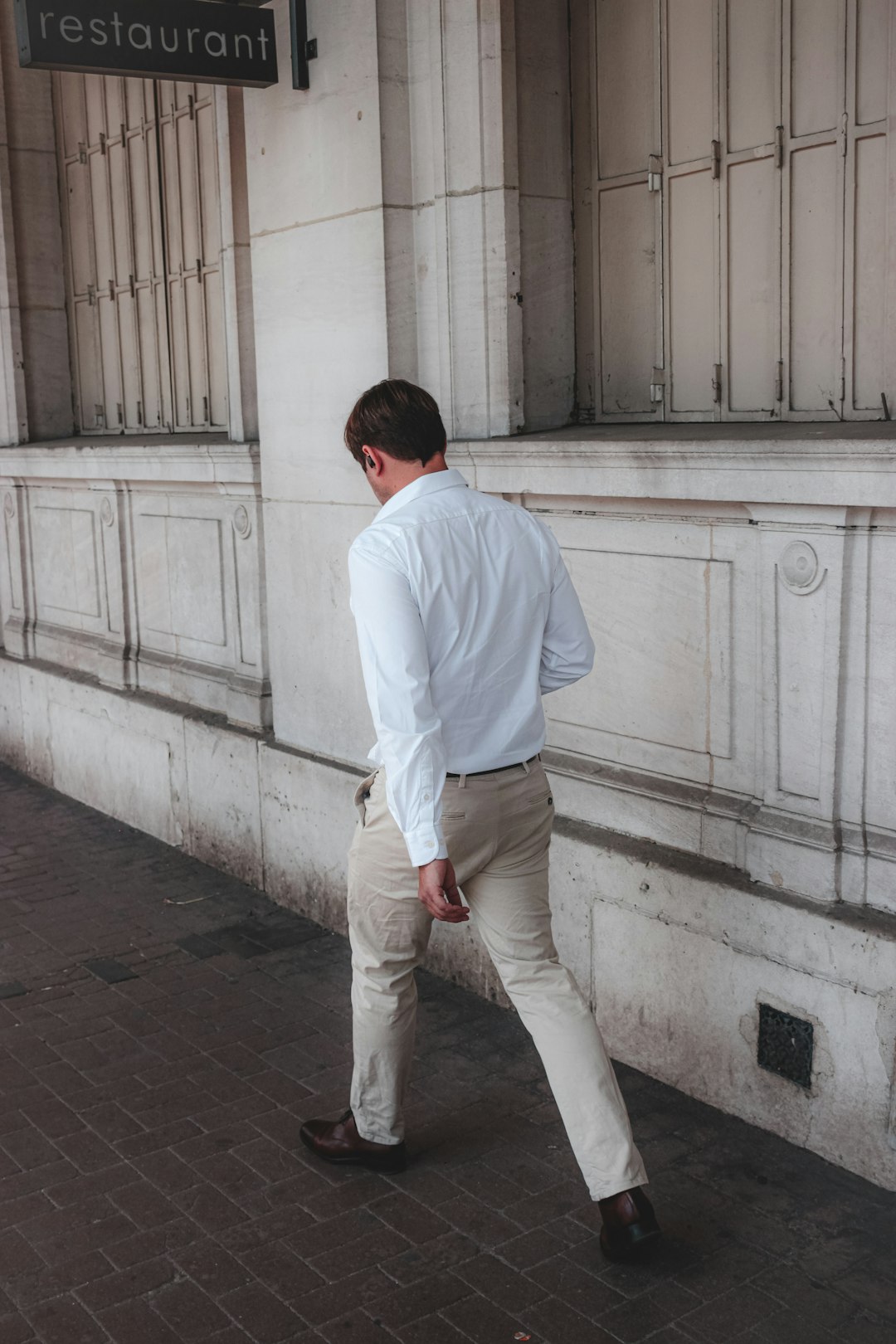 man in white dress shirt and brown pants standing on gray concrete floor during daytime