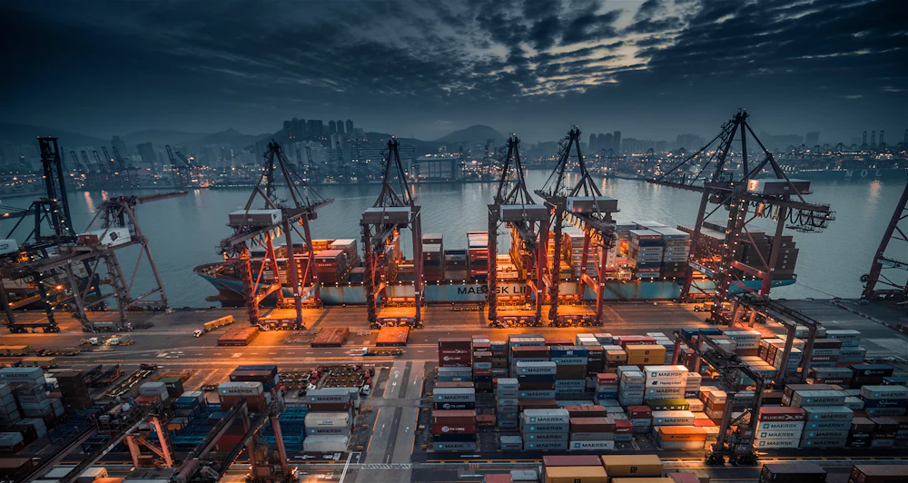 Container ship being loaded by cranes at an industrial port at dusk