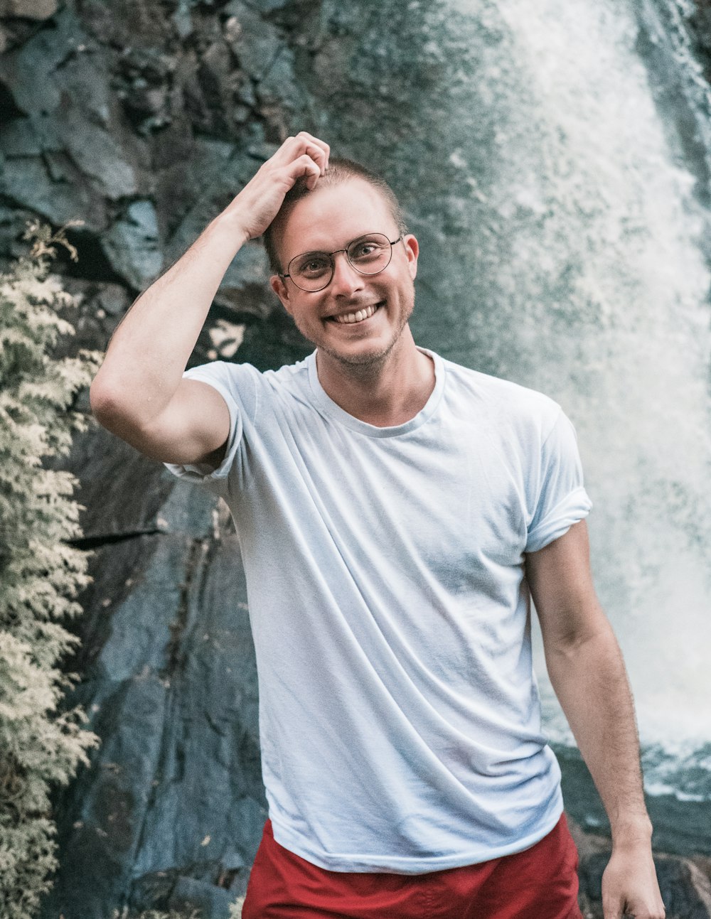 man in white crew neck t-shirt standing near gray rock