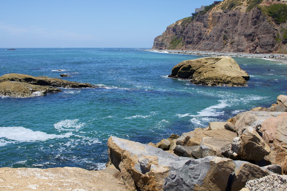 brown rocky mountain beside blue sea during daytime