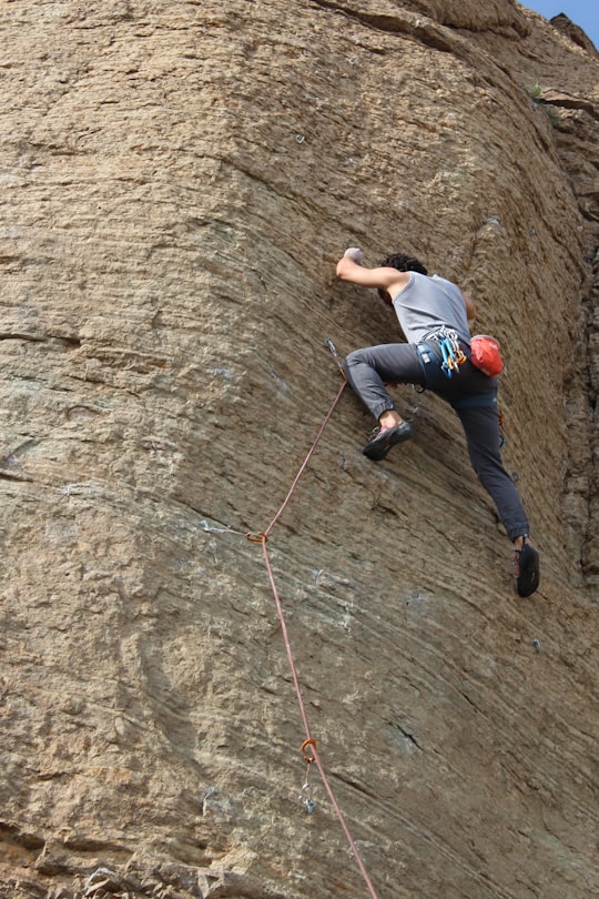 man in blue t-shirt climbing on brown rock in Tehran Iran
