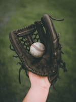person holding baseball ball in black leather baseball mitt