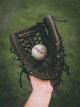 person holding baseball ball in black leather baseball mitt