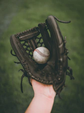 person holding baseball ball in black leather baseball mitt