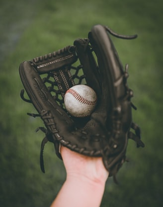 person holding baseball ball in black leather baseball mitt