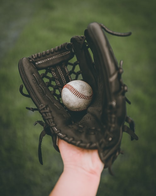 person holding baseball ball in black leather baseball mitt