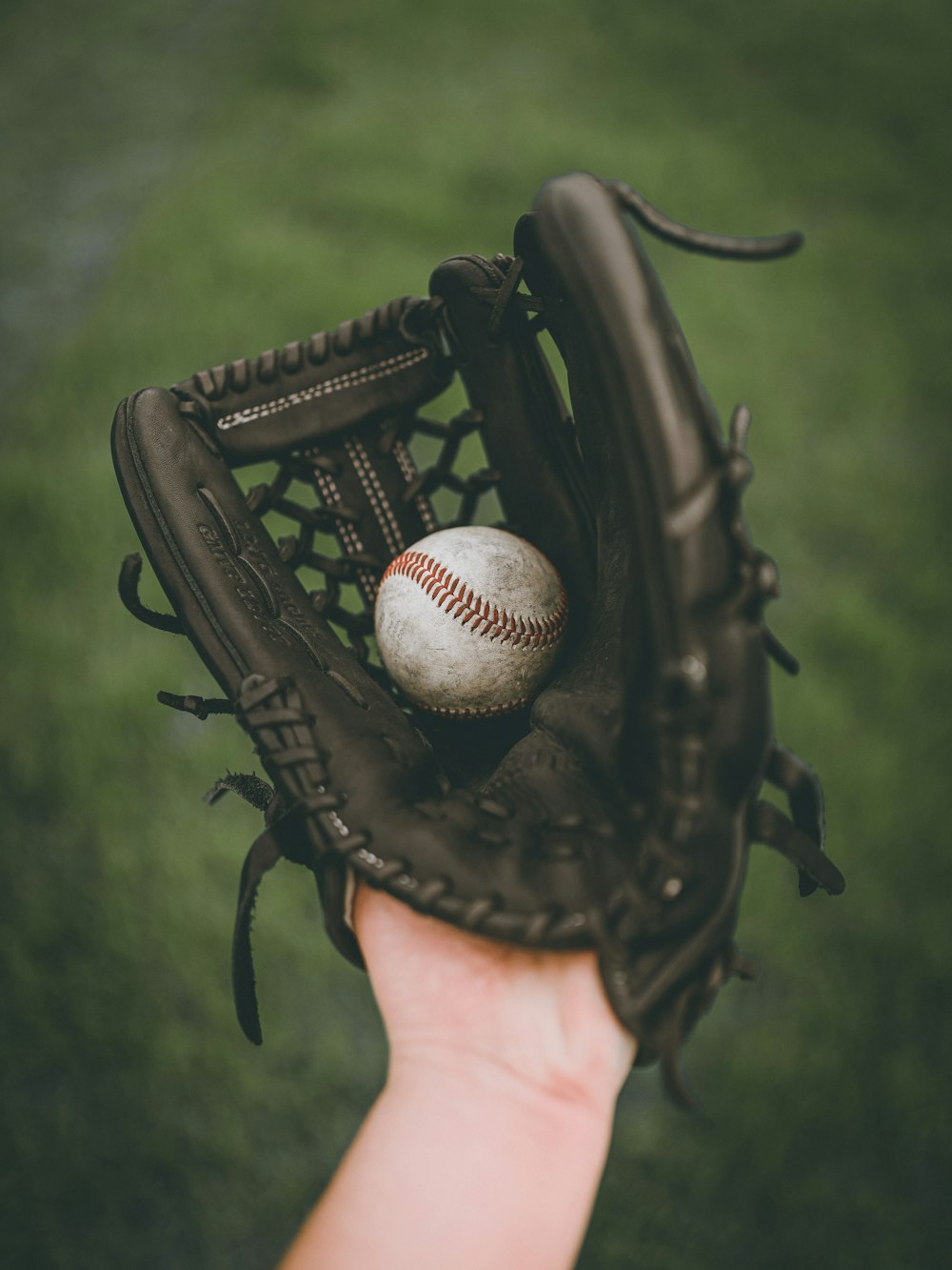 person holding baseball ball in black leather baseball mitt