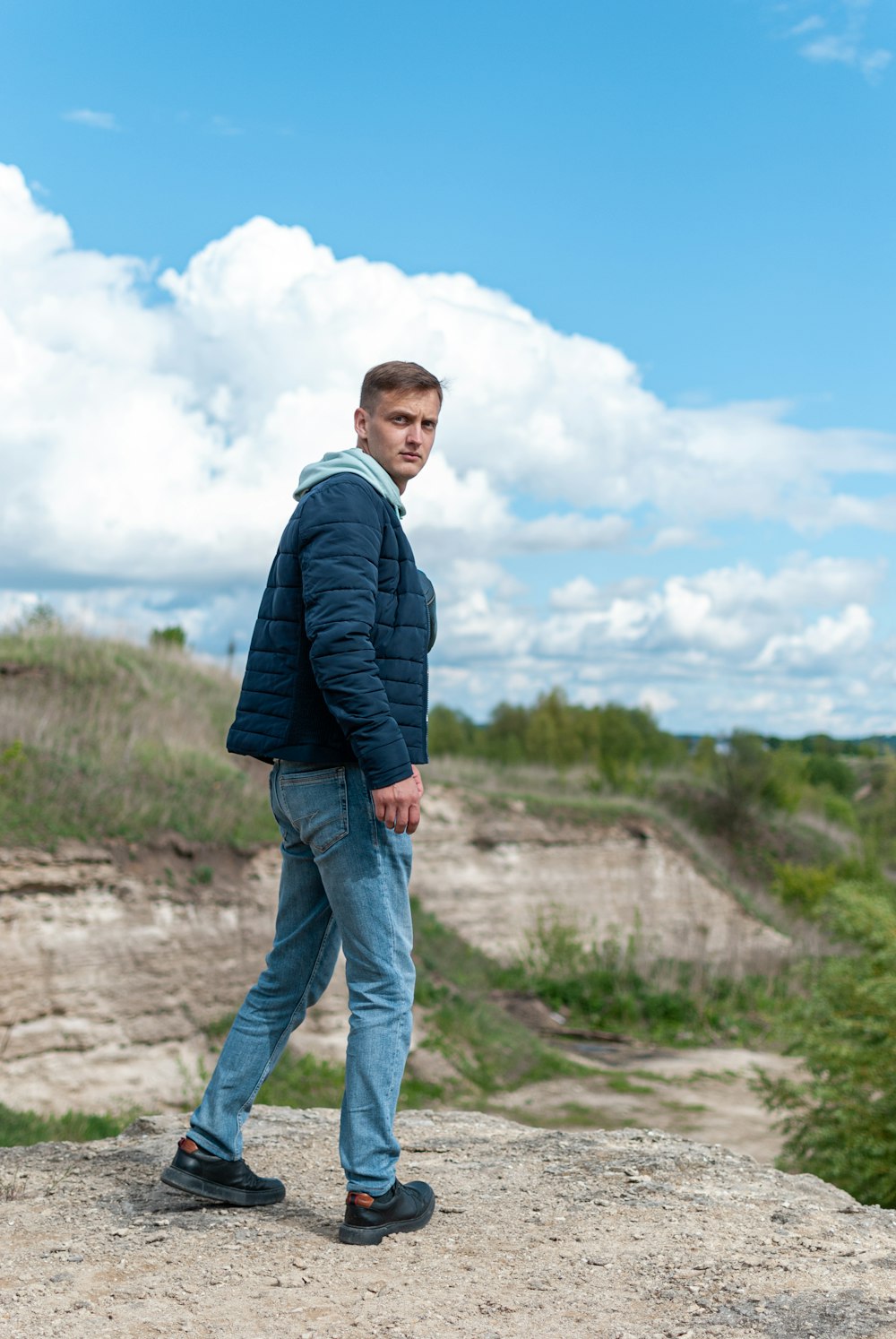 man in black jacket and blue denim jeans standing on brown dirt road during daytime