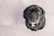 A black dog with expressive eyes is looking up, sitting on a tiled floor. The dog appears to have a graying snout and is wearing a collar.