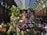 A lush, vertical display of assorted flowers, predominantly pink and white, surrounded by vibrant green foliage. This floral arrangement is set against an elegant arched indoor setting with a glass-paneled ceiling and ornate metal structures, providing a charming contrast between nature and architecture.