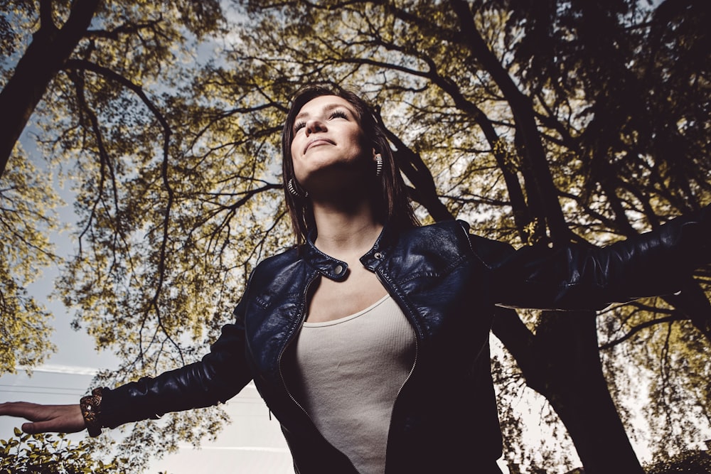 woman in black leather jacket standing near trees during daytime