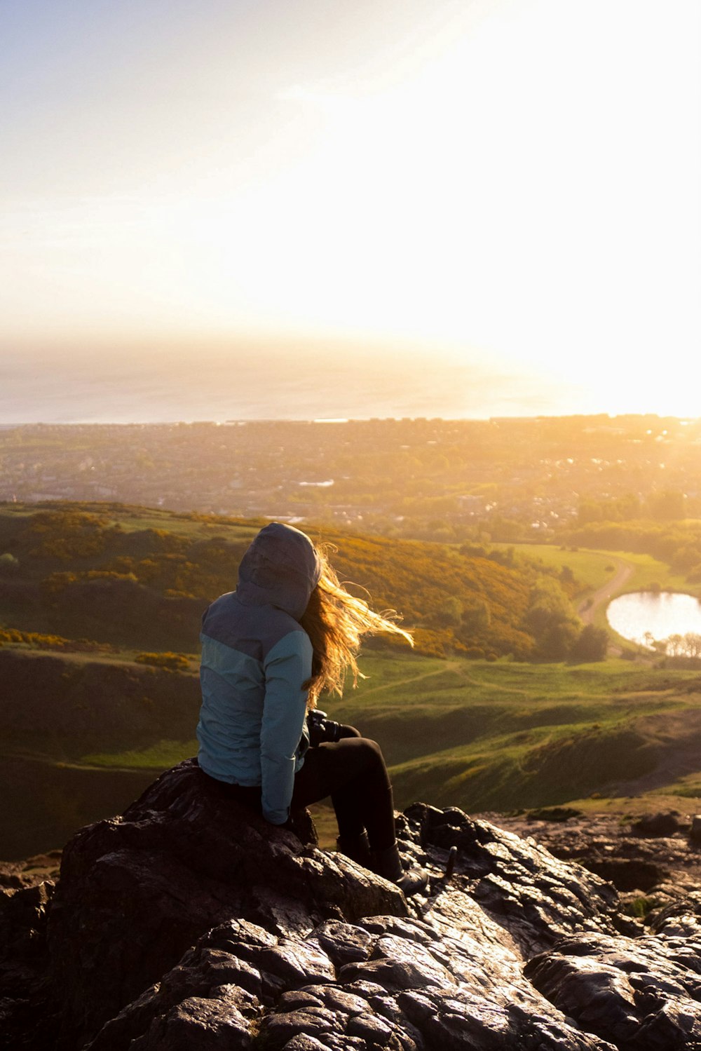 woman in gray hoodie sitting on rock during daytime