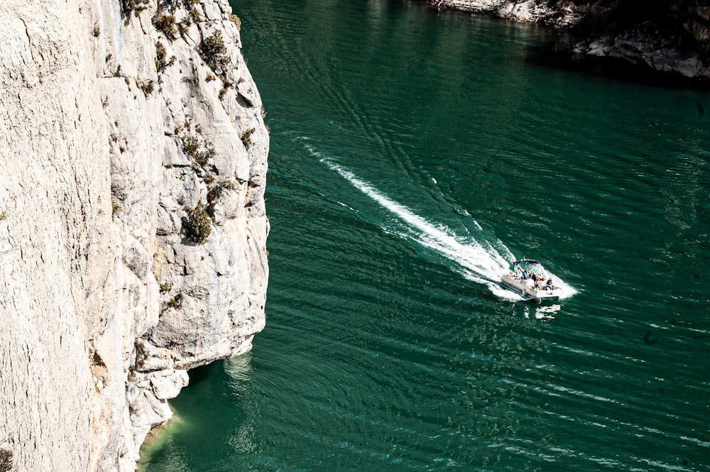 white boat on sea beside rocky mountain during daytime