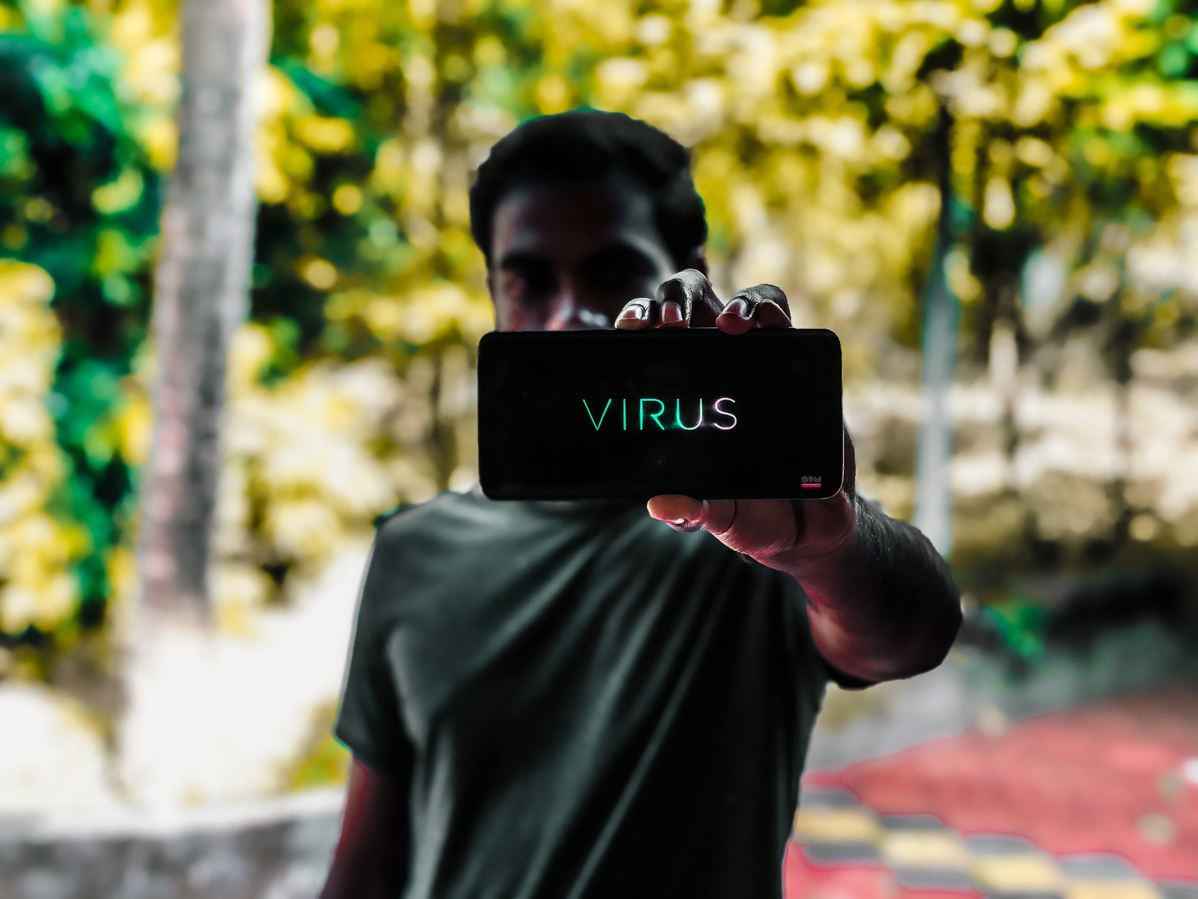 青いクルーネックTシャツを着た男が黒いスマートフォンを持っている