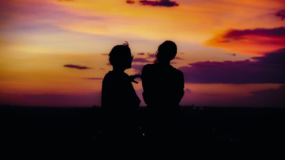 Silueta de 2 personas de pie durante la puesta del sol