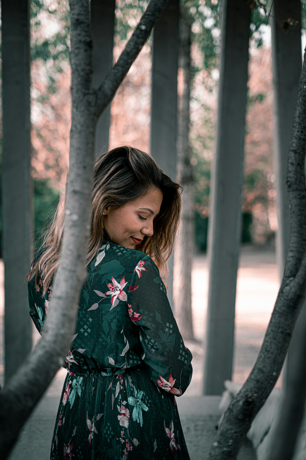 낮 동안 갈색 나무 근처에 서 있는 검은색과 빨간색 꽃무늬 긴팔 셔츠를 입은 소녀