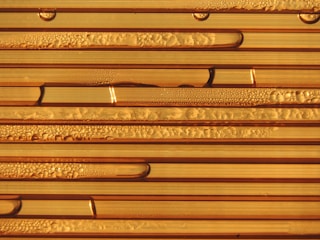 Close-up view of condensation forming droplets on the surface of striped, translucent tubes. The droplets vary in size and are distributed unevenly, creating patterns of texture and light reflection.