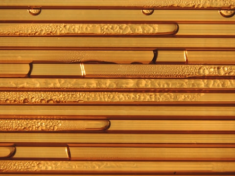 Close-up view of condensation forming droplets on the surface of striped, translucent tubes. The droplets vary in size and are distributed unevenly, creating patterns of texture and light reflection.
