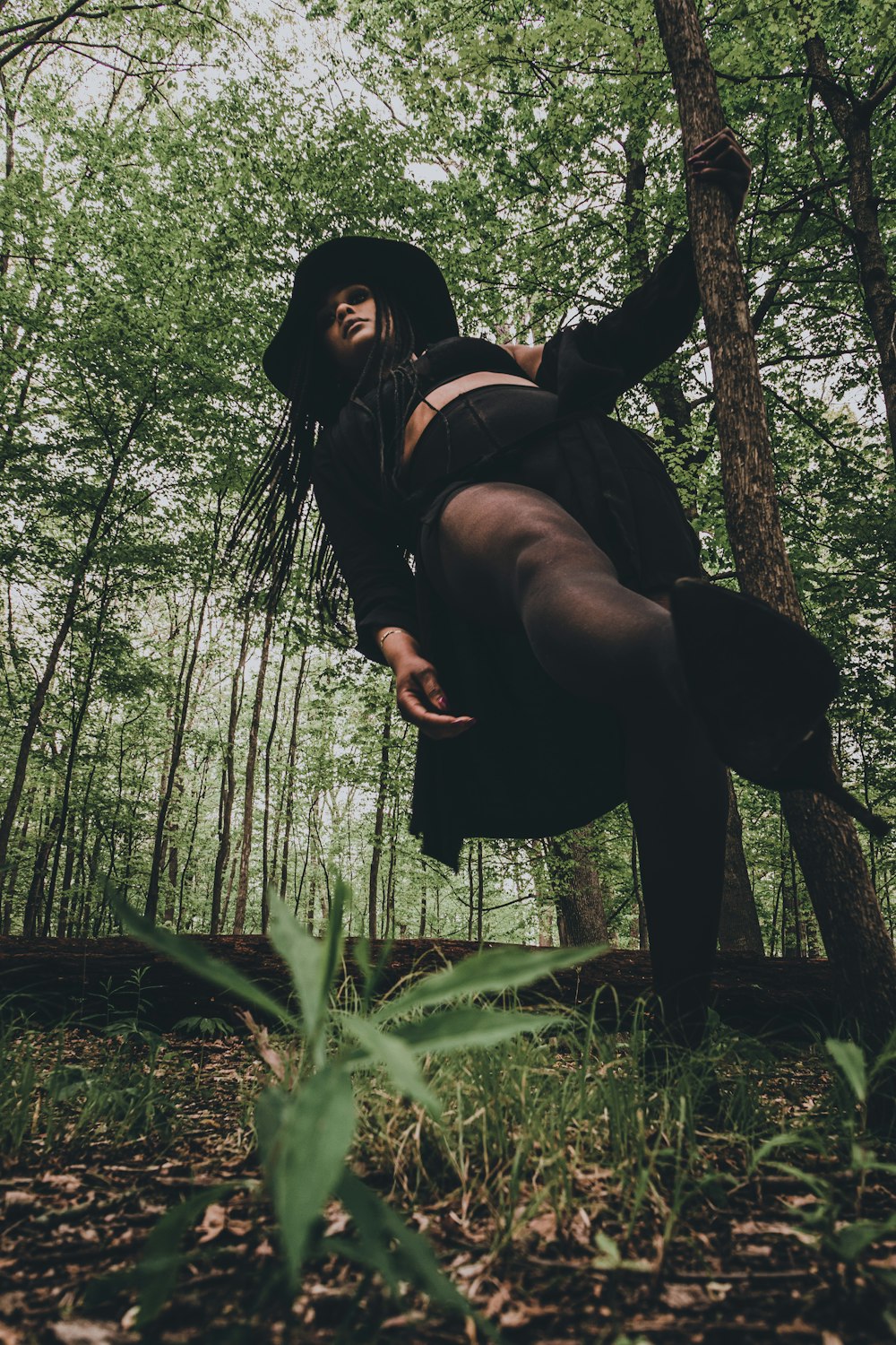 a woman in a black dress and hat in the woods