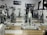 A room filled with stationary exercise bikes arranged neatly in rows. The space has a wooden and gray tiled floor, and a sign with the text 'i-Fitness' is displayed on the wall. The bikes are primarily white with black handlebars and seats.