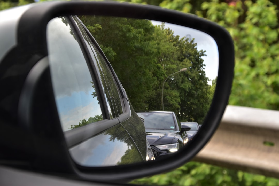 black car side mirror reflecting green trees during daytime