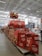 A large warehouse with high ceilings and bright lighting contains a neatly organized section of Nestlé chocolate products. Stacks of red and brown packaging are prominently displayed on shelves and pallets. Promotional signs and banners advertising the chocolate collection are visible.