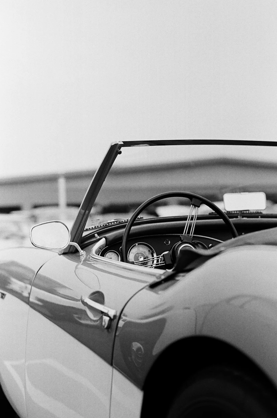 Black and white view of a classic open car cabin with a large period steering wheel