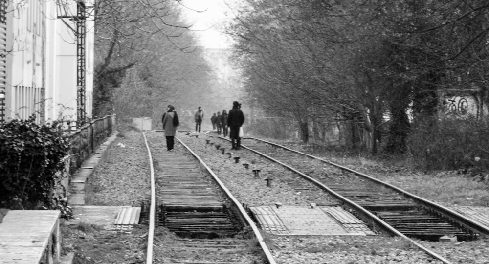 grayscale photo of people walking on train rail