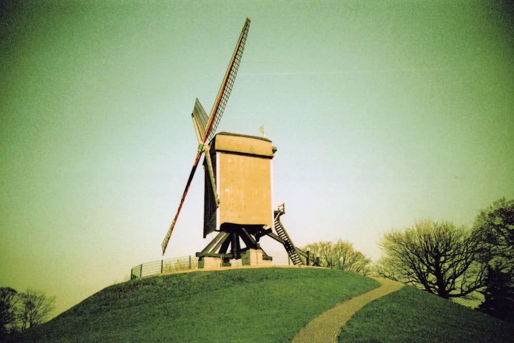 brown windmill on green grass field under gray sky
