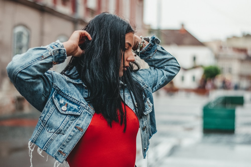 woman in blue denim jacket and red shirt covering face with hair