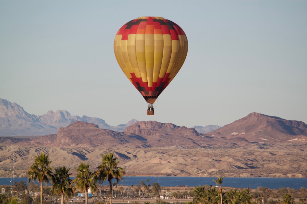 red and yellow hot air balloon flying over the green trees during daytime