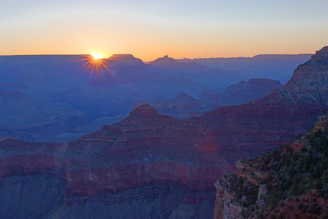 A stunning sunrise over the colorful cliffs of the Yellowstone Grand Canyon rim, with a winding trail visible.