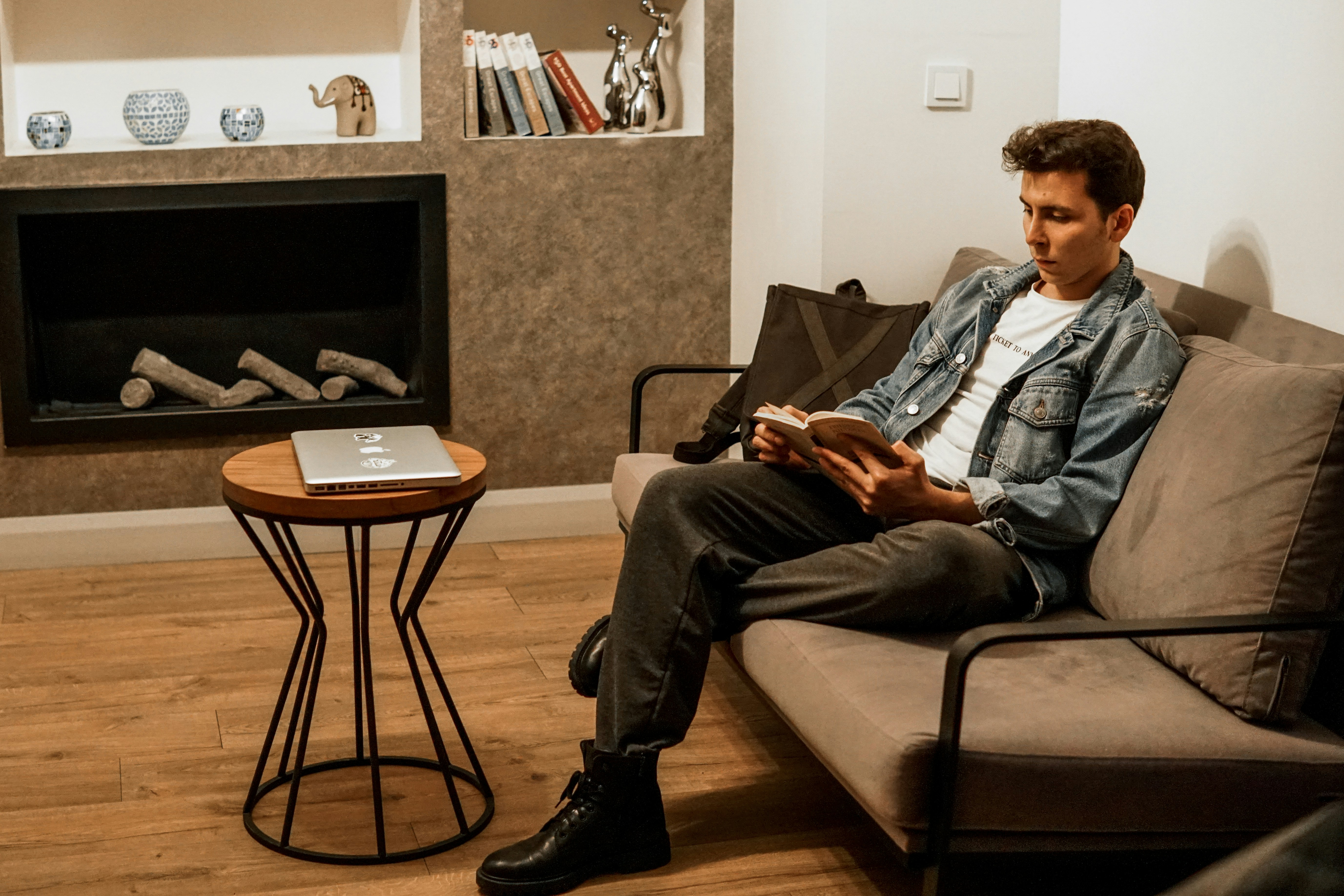 man in blue denim jacket and black pants sitting on black sofa chair