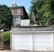 A brick house with a double garage is adorned with a handmade sign that reads 'Thank U to those who risk their life for us.' An American flag is displayed prominently beside the sign, and the house is surrounded by lush green trees and plants.