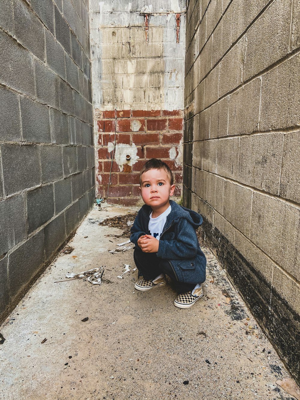 boy in blue jacket sitting on brown brick wall