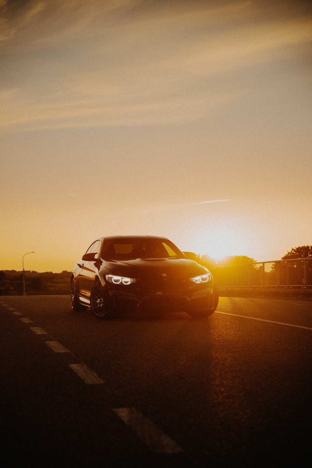 a black car driving down a road at sunset