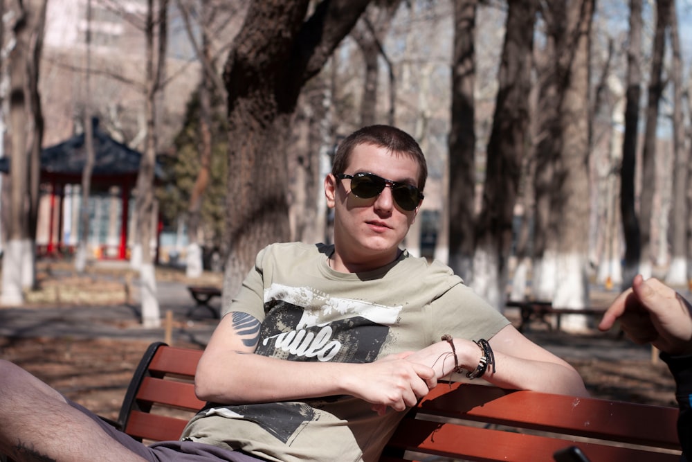 man in black sunglasses and gray and black long sleeve shirt sitting on brown wooden bench