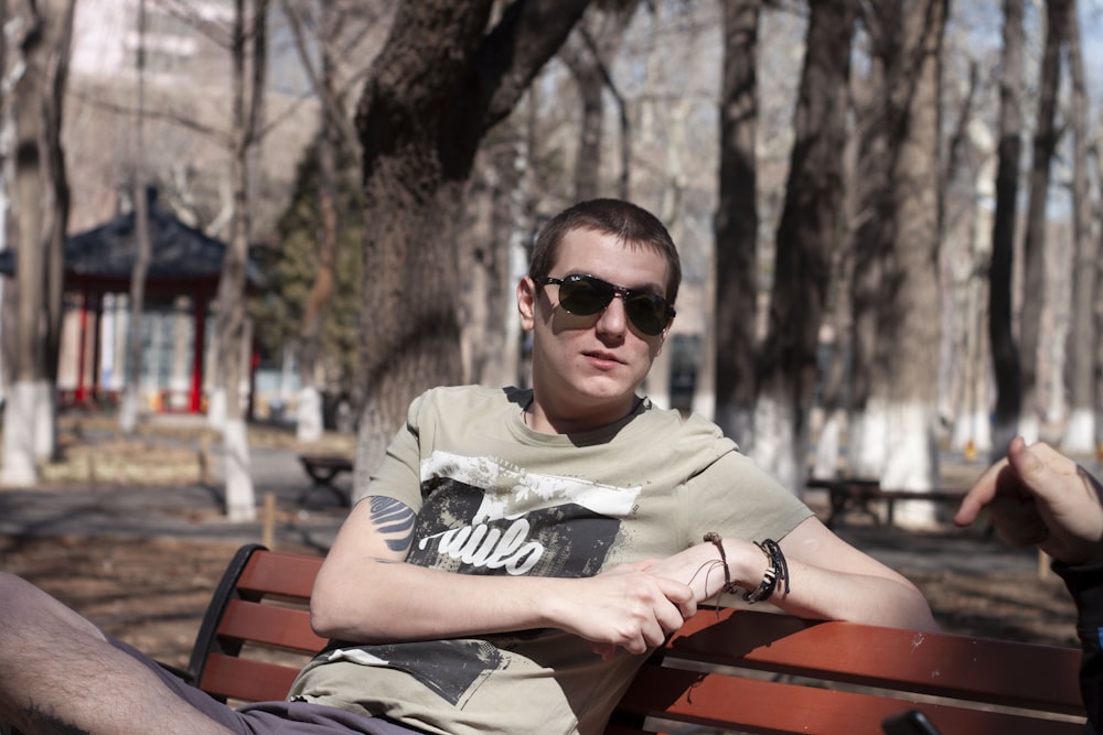 man in black sunglasses and gray and black long sleeve shirt sitting on brown wooden bench