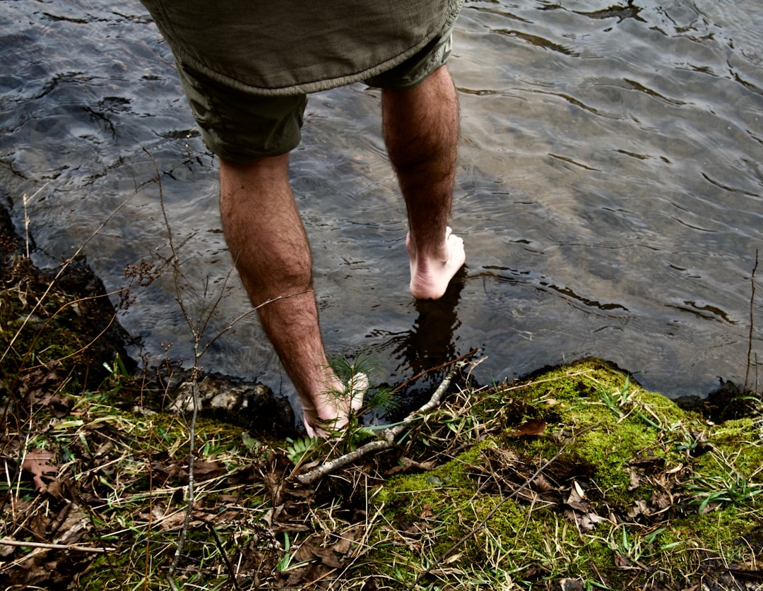 man in green shorts standing on green grass near body of water during daytime