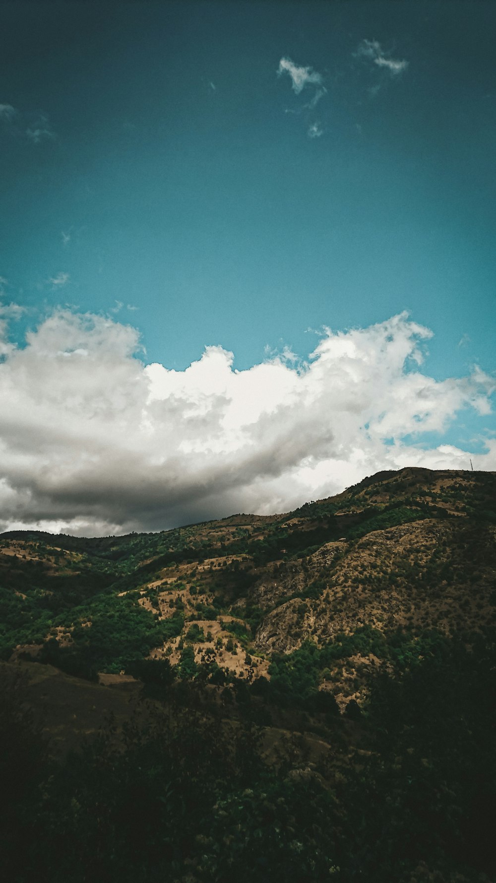 montaña verde y marrón bajo el cielo azul y nubes blancas durante el día