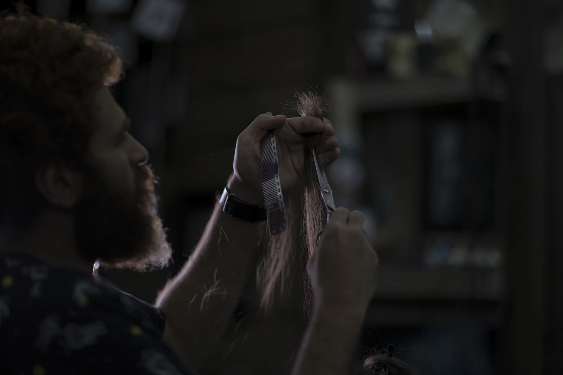 A moody, close-up shot of a barber's hands skillfully trimming a client's beard with vintage scissors, set against a dark, textured background.